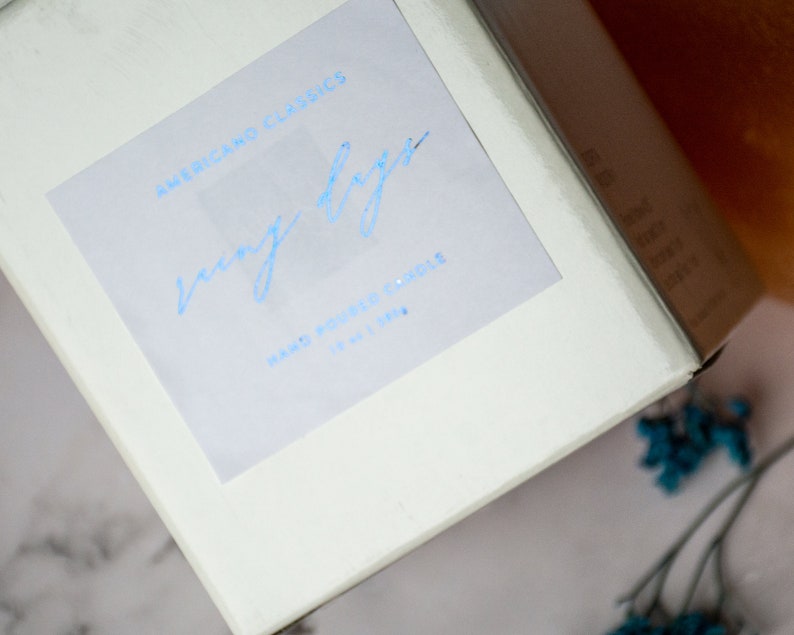 May include: White candle box with a blue label that says "Americano Classics" and "cozy days" in a handwritten font. The label also says "Hand Poured Candle 10 oz 140 hr."
