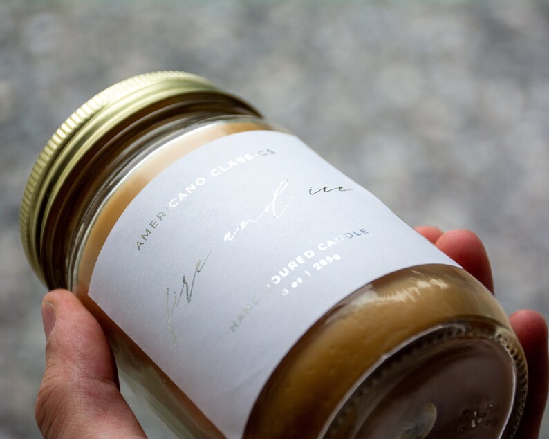 May include: A white candle jar with a gold lid. The label reads "Americano Classics" and "Fire and Ice" in silver lettering. The label also says "Hand-poured candle" and "oz | 283g".