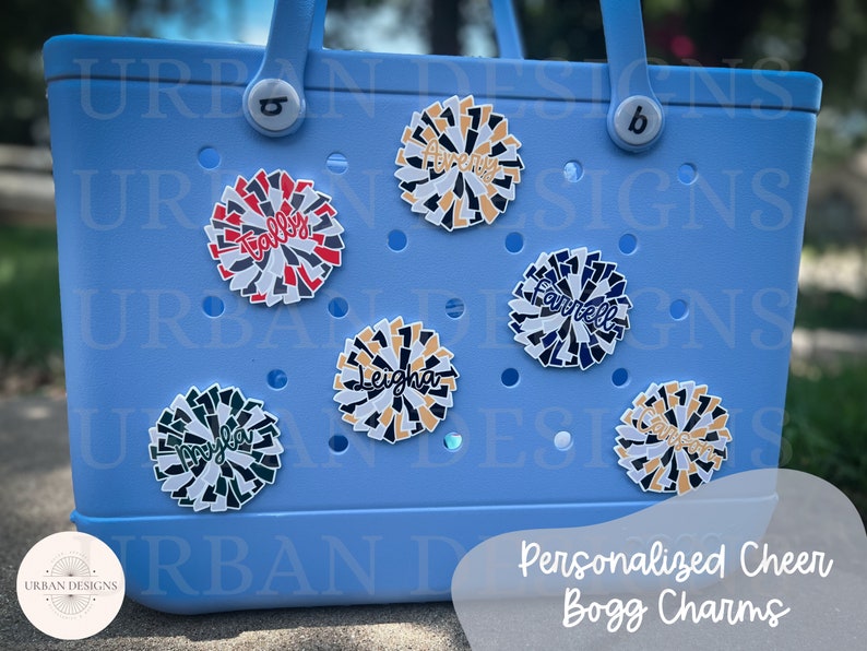 May include: A light blue tote bag with personalized cheer pom-pom charms. The charms are decorated with different colors and names, including "Tally", "Leigha", "Farrell", and "Cameron".