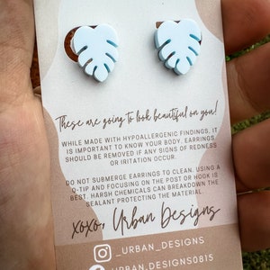 May include: A pair of light blue monstera leaf earrings with a white background. The card includes the text "These are going to look beautiful on you!" and "xoxo, Urban Designs".