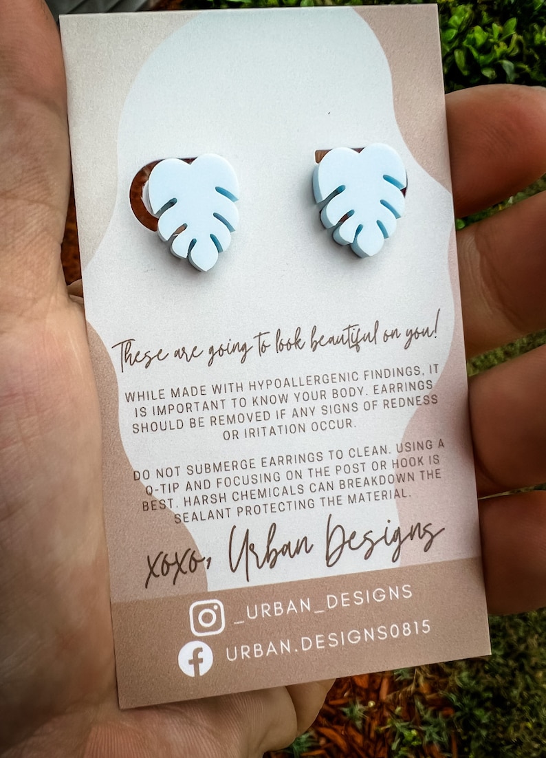 May include: A pair of light blue monstera leaf earrings with a white background. The card includes the text "These are going to look beautiful on you!" and "xoxo, Urban Designs".