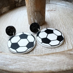 May include: A pair of black and white soccer ball earrings with black glitter accents. The earrings are made of polymer clay and are lightweight and easy to wear.