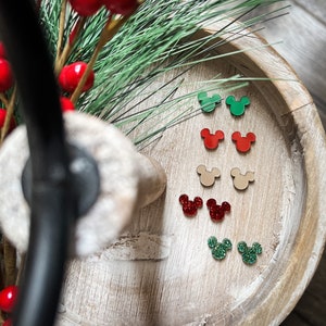 Peut inclure: Un ensemble de six paires de boucles d'oreilles en forme d'oreilles de souris à paillettes, en rouge, vert et beige. Les boucles d'oreilles sont disposées par paires sur un plateau en bois.