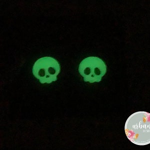 May include: Two green glow-in-the-dark skull earrings. The skulls have a simple design with two eye sockets and a nose.