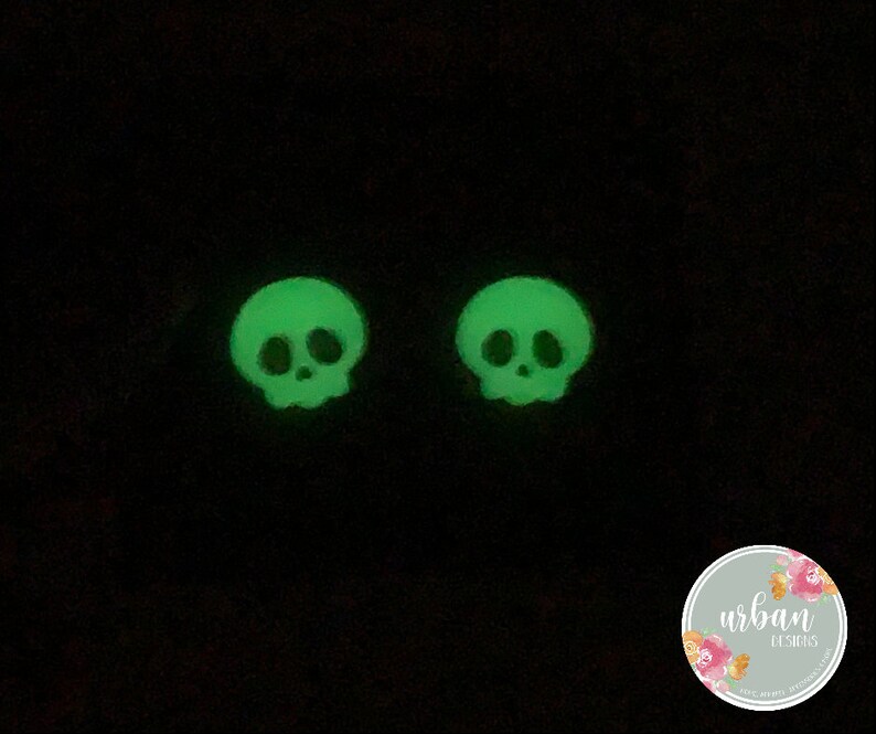 May include: Two green glow-in-the-dark skull earrings. The skulls have a simple design with two eye sockets and a nose.