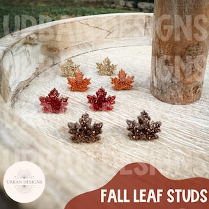 May include: A collection of fall leaf studs in various colors, including gold, orange, red, and brown. The studs are arranged on a wooden surface. The text "FALL LEAF STUDS" is visible at the bottom of the image.