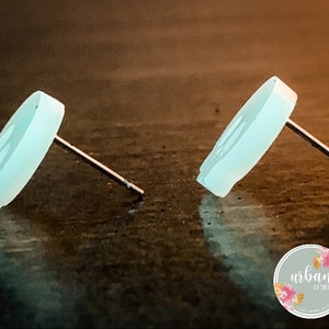 May include: A pair of light blue skull stud earrings. The earrings are made of a smooth, opaque material and have a simple, minimalist design.