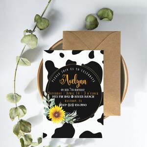 May include: A birthday invitation with a cow print background and a gold-rimmed circle. The circle contains the name "Avelynn" in gold script, along with event details and a sunflower illustration. A brown envelope is included.