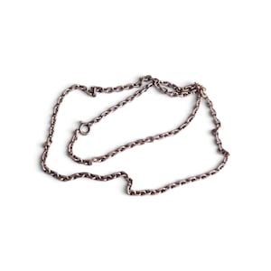 Op de afbeelding: Een zilverkleurige metalen ketting bestaande uit een reeks onderling verbonden ovale schakels. De ketting is gerangschikt in een losse, overlappende lus en bevat een kleine ronde veerringsluiting om de uiteinden aan elkaar te bevestigen.