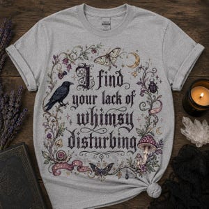 Może przedstawiać: Szary melanżowy t-shirt z czarnym nadrukiem graficznym z tekstem I find your lack of whimsy disturbing. Wzór zawiera kruka, ćmę, chrząszcza, ślimaka, grzyba, półksiężyc oraz kwiatowe pnącza otaczające napis.