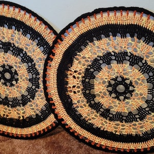 May include: Two black and orange crocheted doilies with a circular design.