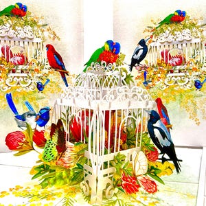 May include: A white paper art piece featuring several colorful birds perched around white birdcages. The birds are red, blue, green, and black, with yellow and red flowers and foliage.
