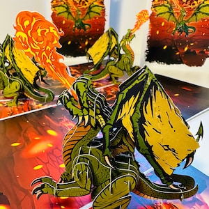 May include: A three-dimensional pop-up card featuring a green dragon breathing fire. The dragon has detailed wings and scales, set against a fiery background. Additional cards show dragons in flight, creating a fantasy scene.