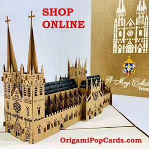 May include: A brown paper pop-up card depicting St. Mary's Cathedral in Sydney, Australia. The card is open and the cathedral is fully extended. The card is made of paper and has a brown and white color scheme. The card is on a white surface. The text "SHOP ONLINE" is in red letters at the top of the image. The text "OrigamiPopCards.com" is at the bottom of the image.