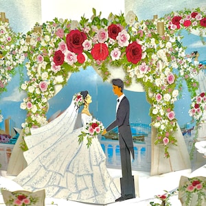 May include: A pop-up wedding scene with a bride and groom under a floral archway. The arch is adorned with red and pink roses, white flowers, and greenery. The bride wears a white gown and veil, holding a bouquet. The groom wears a tuxedo.