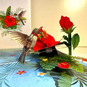 Tarjeta de felicitación 3D emergente de feliz cumpleaños con un colibrí que atrae flores de hibisco rojo. Tienda de tarjetas pop-up de origami en línea: https://origamipopcards.com