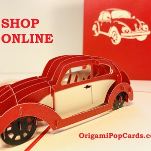 May include: A red and white 3D pop-up card featuring a vintage Volkswagen Beetle. The card is open and the car is partially extended. The text "SHOP ONLINE" is printed on the front of the card. The website "OrigamiPopCards.com" is printed on the bottom of the card.