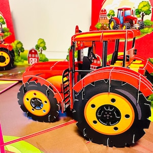Puede incluir: Una tarjeta emergente roja y negra con un tractor rojo con un asiento de conductor negro y ruedas amarillas. La tarjeta está abierta y el tractor está parcialmente extendido.
