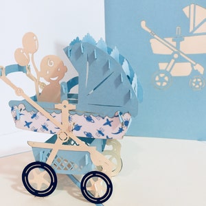 May include: A blue and white papercraft pop-up card featuring a baby in a stroller with balloons. The card is open and the stroller is in the foreground. The background is a light blue color.