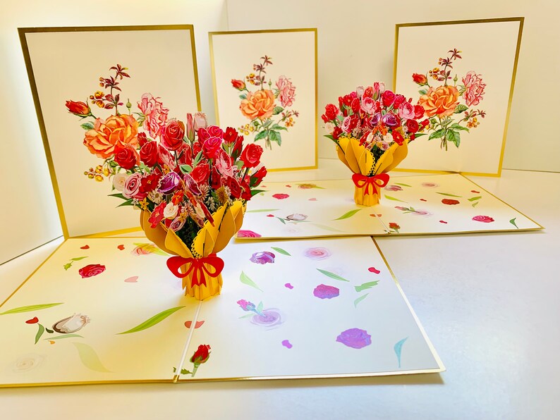 May include: Three pop-up cards with a bouquet of red, pink, and white flowers in a yellow paper wrapper with a red bow. The cards are open and the flowers are in 3D.