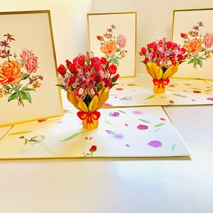May include: Three pop-up cards with a bouquet of pink, red, and white roses in a yellow vase. The cards are open and the roses are in 3D. The cards have a gold border and a white background.