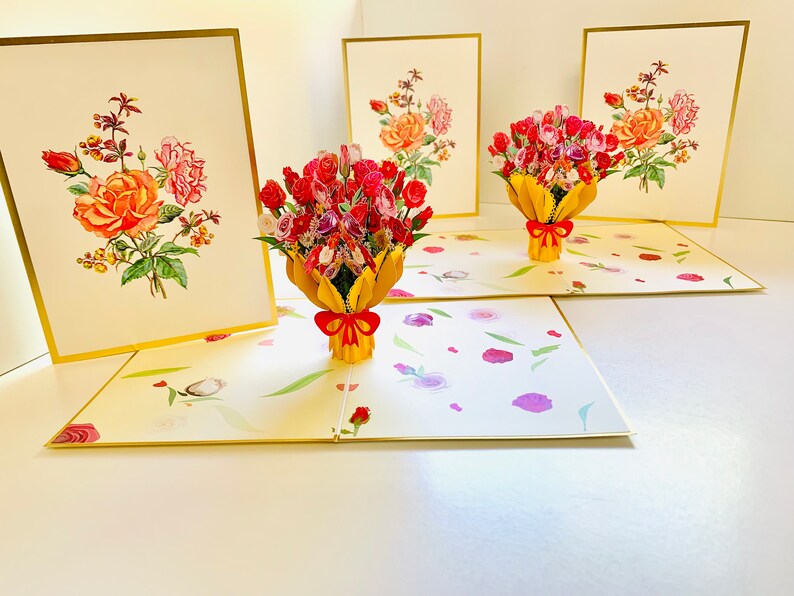 May include: Three pop-up cards with a bouquet of pink, red, and white roses in a yellow vase. The cards are open and the roses are in 3D. The cards have a gold border and a white background.