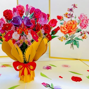 May include: A 3D pop-up card featuring a bouquet of colorful flowers in a yellow paper wrapper with a red bow. The card is open and the flowers are in focus. The background is a light yellow with a floral pattern.