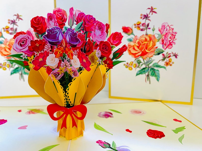 May include: A 3D pop-up card featuring a bouquet of colorful flowers in a yellow paper wrapper with a red bow. The card is open and the flowers are in focus. The background is a light yellow with a floral pattern.