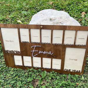 May include: A wooden baby milestone photo frame with spaces for photos from newborn to one year. The frame is stained dark brown with the name "Emma Grace" in a lighter color. The frame has spaces for 12 photos.