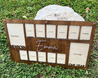 May include: A wooden photo frame with 12 spaces for pictures, designed to track a baby's growth from newborn to one year old. The frame is brown with a light wood interior and has the name "Emma Grace" engraved on it.
