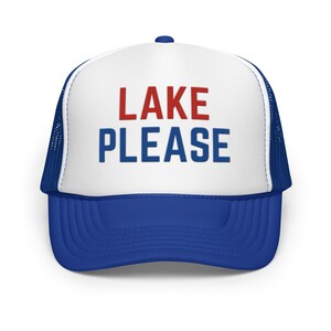 Op de afbeelding: Een blauw-witte truckerpet met een wit voorpaneel met de tekst LAKE in het rood en PLEASE in het blauw. De pet heeft een blauwe klep en blauwe mesh achterpanelen, met een gestructureerde kroon en een knoopje aan de bovenkant.