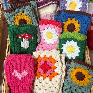 May include: A basket filled with crocheted and knitted pot holders in various colors and patterns, including sunflowers, daisies, and mushrooms. The pot holders are made with different types of yarn and have a variety of textures.