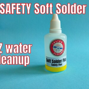 以下が含まれることがあります： 「Soft Solder Flux Safety Flux」と書いてある黄色のラベルが付いた透明な軟ろう付けフラックスのボトルです。ボトルには、「Lustro Electro」と書かれた赤い円があり、円の中に稲妻と拳があります。ボトルは薄い青色の背景の上に置かれています。