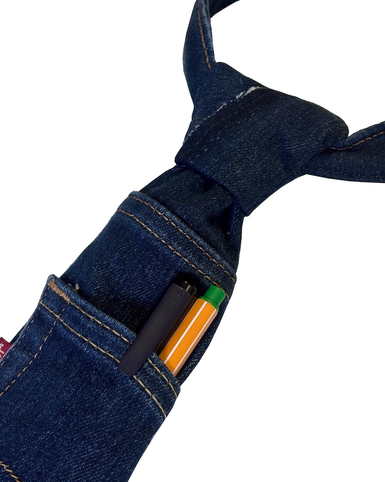 K&ouml;nnte beinhalten: Eine dunkelblaue Jeans-Krawatte mit einer Tasche, die einen schwarzen Stift und einen orangefarbenen Textmarker enth&auml;lt. Die Krawatte ist aus Jeansstoff gefertigt und hat einen klassischen Knoten. Die Tasche ist mit einem Kontrastfaden gen&auml;ht.