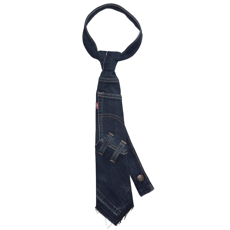 K&ouml;nnte beinhalten: Eine dunkelblaue Jeans-Krawatte mit einzigartigem Design. Die Krawatte scheint aus recycelten Jeans gefertigt zu sein, mit Taschen-Details und einem Knopfverschluss. Das rote Levi's-Etikett ist sichtbar.