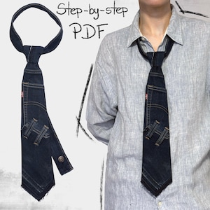 Puede incluir: Una corbata de mezclilla azul oscuro con un diseño único, con los detalles de bolsillo y costura de los jeans. La corbata tiene un cierre de botón y una etiqueta roja. El texto "Step-by-step PDF" es visible.