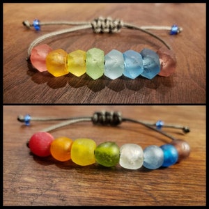 May include: Two rainbow colored bracelets with gray string and blue beads. The bracelets are made with glass beads in various colors, including red, orange, yellow, green, blue, and purple.