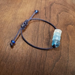 May include: A dark blue cord bracelet with a stack of three blue and white glass beads.
