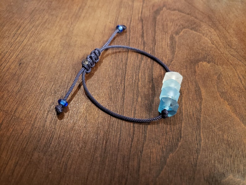 May include: A dark blue cord bracelet with a stack of three blue and white glass beads.