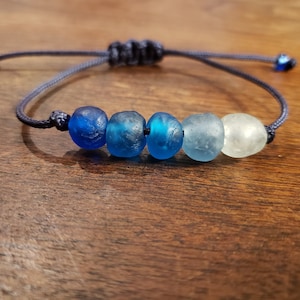 May include: A blue and white glass bead bracelet with a dark blue cord. The beads are graduated in color from dark blue to light blue to white.