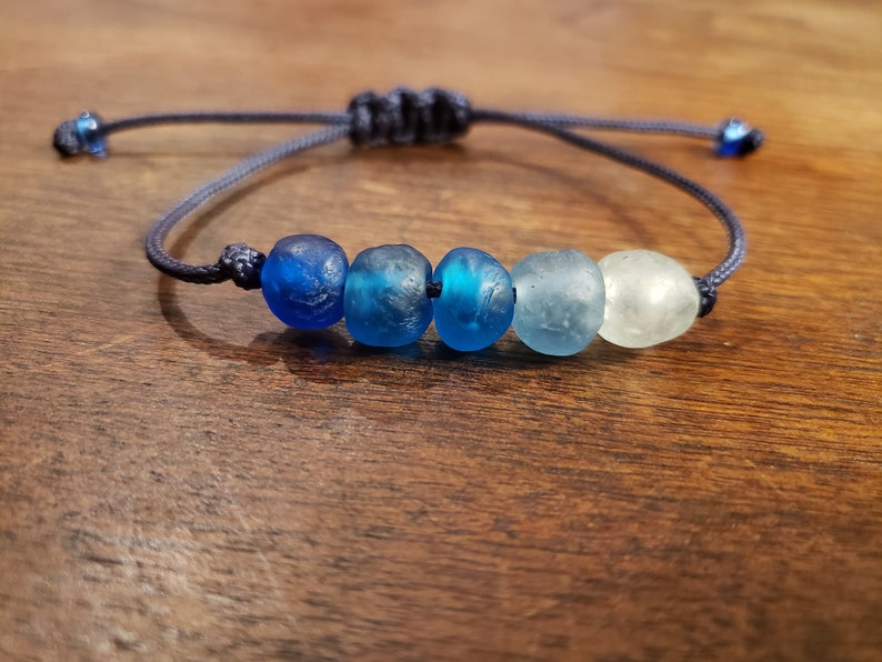 May include: A blue and white glass bead bracelet with a dark blue cord. The beads are graduated in color from dark blue to light blue to white.