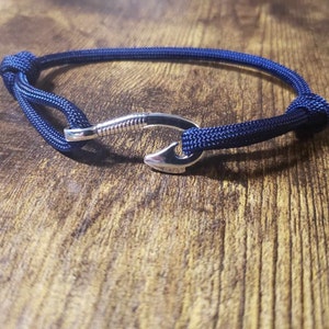 May include: A navy blue paracord bracelet with a silver fishing hook clasp.