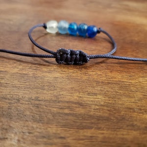 May include: A blue and white beaded bracelet with a dark blue cord and a knot closure.