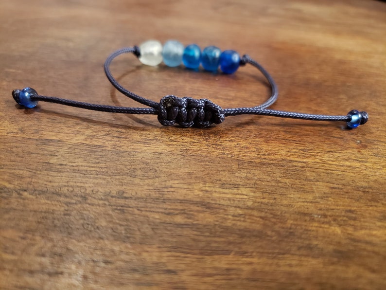 May include: A blue and white beaded bracelet with a dark blue cord and a knot closure.