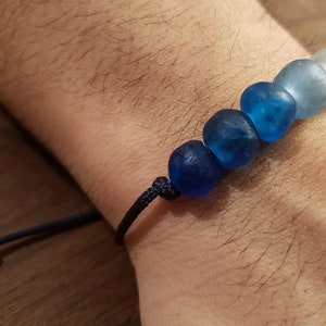 May include: A blue and white glass bead bracelet with a dark blue cord. The beads are graduated in size, with the largest bead at the bottom and the smallest bead at the top.