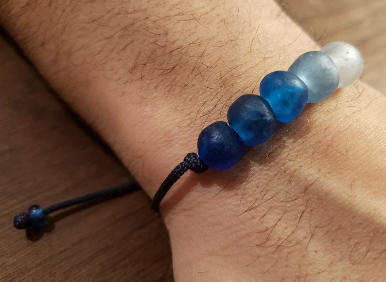 May include: A blue and white glass bead bracelet with a dark blue cord. The beads are graduated in size, with the largest bead at the bottom and the smallest bead at the top.