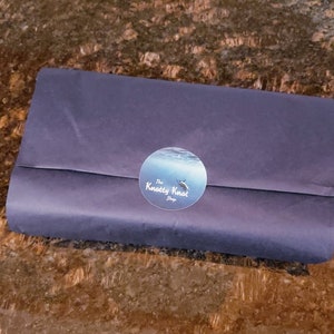 May include: A blue and white sticker with the text "The Knotty Knot Shop" on a dark blue paper package.