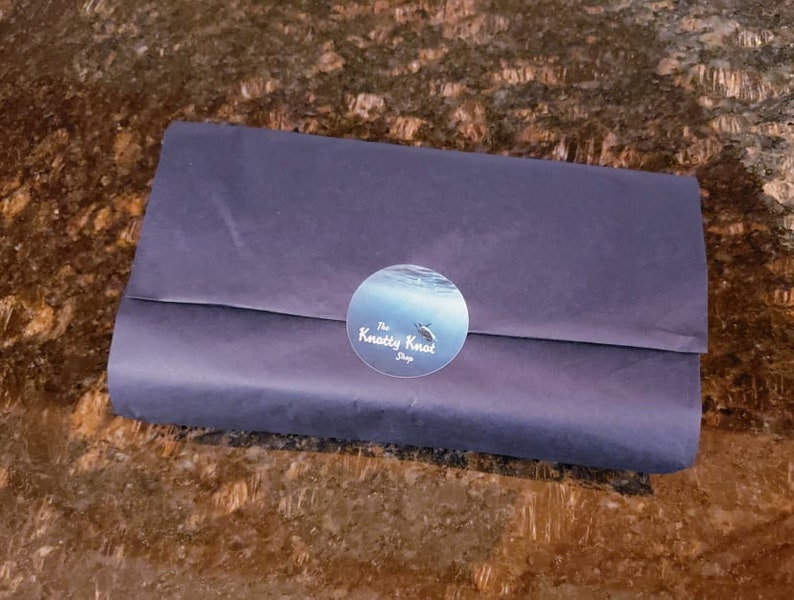 May include: A blue and white sticker with the text "The Knotty Knot Shop" on a dark blue paper package.