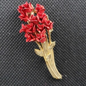 May include: A gold-toned brooch featuring a bouquet of red enamel flowers with green leaves.