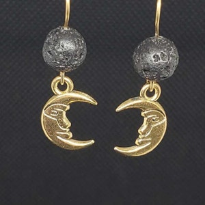 May include: A pair of gold crescent moon earrings with a face design. Each earring features a black lava rock bead.